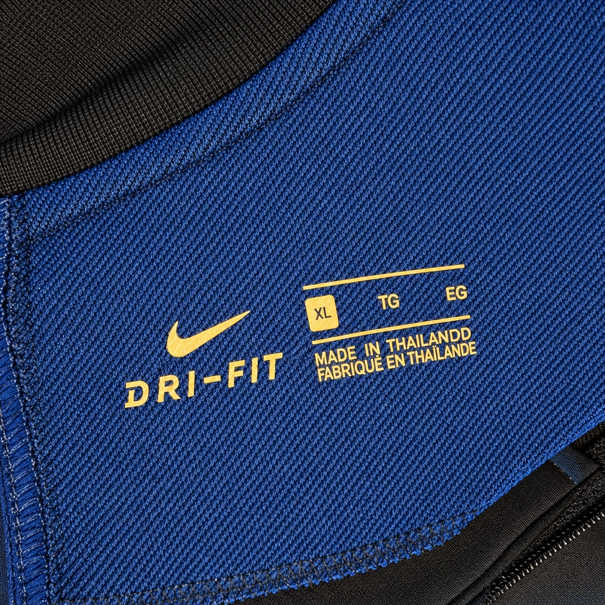 Close-up of a blue athletic garment with yellow printed DRI-FIT branding, size information, and a black zipper edge visible.