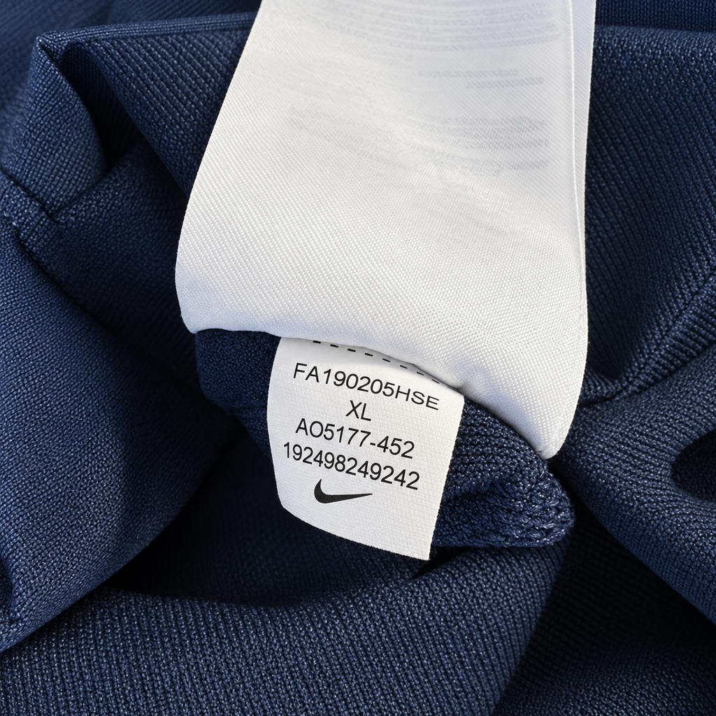 Close-up of a navy blue fabric garment tag with printed size and style information, shown against matching navy fabric.