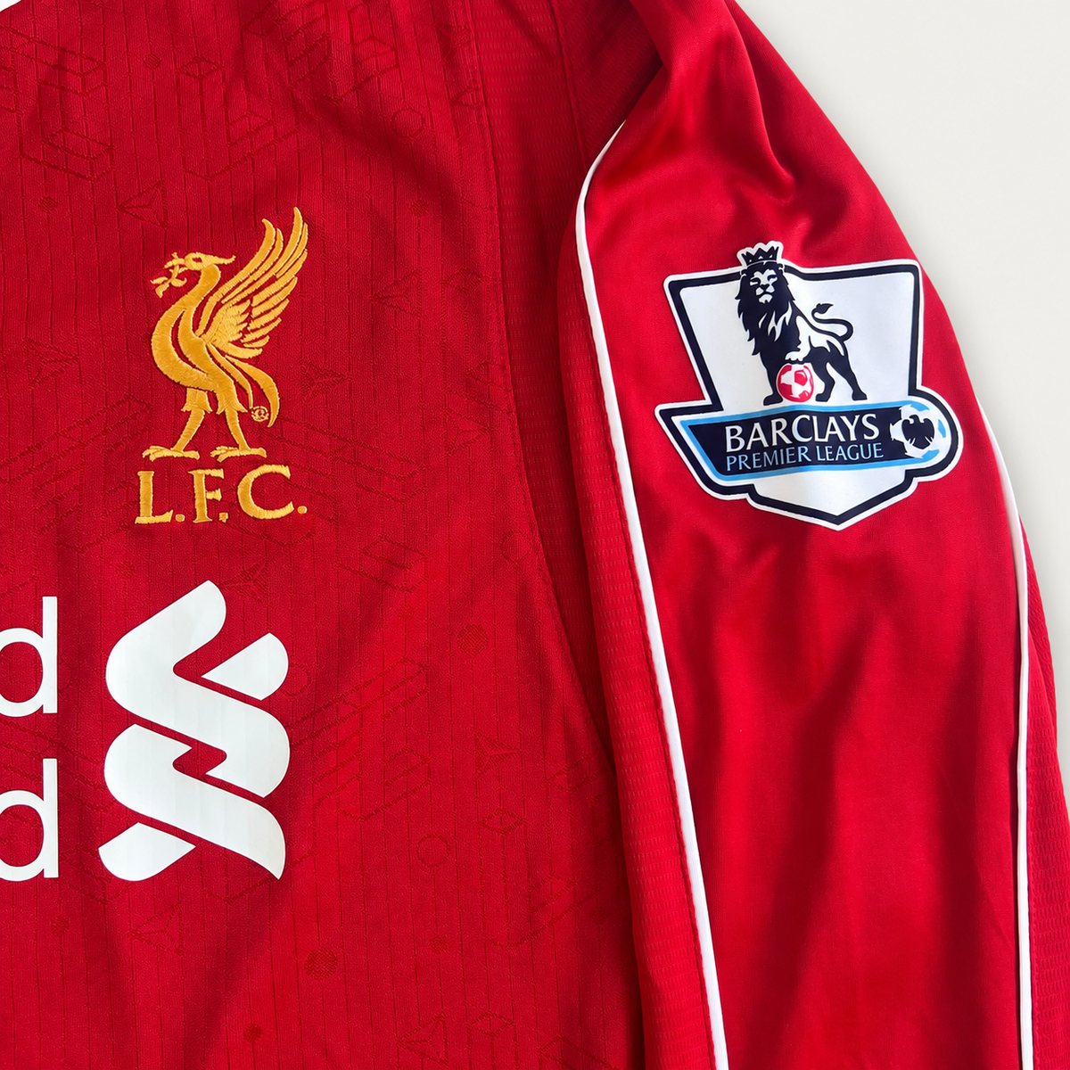 Close-up of a red Liverpool football jersey sleeve and chest area, showing the gold L.F.