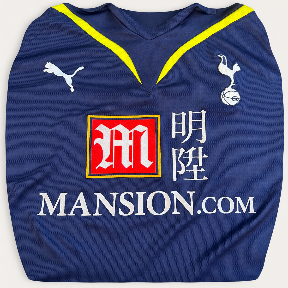 A navy blue soccer jersey laid flat, featuring the white Puma logo, a red and yellow sponsor logo, white Chinese characters, and 'MANSION.COM' printed vertically on the back.