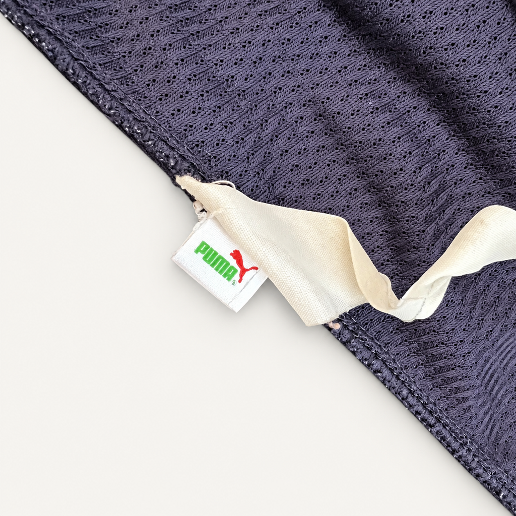 Close-up of a dark navy mesh fabric product with a white fabric tab and a visible Puma tag featuring the green Puma wordmark and red leaping cat logo.