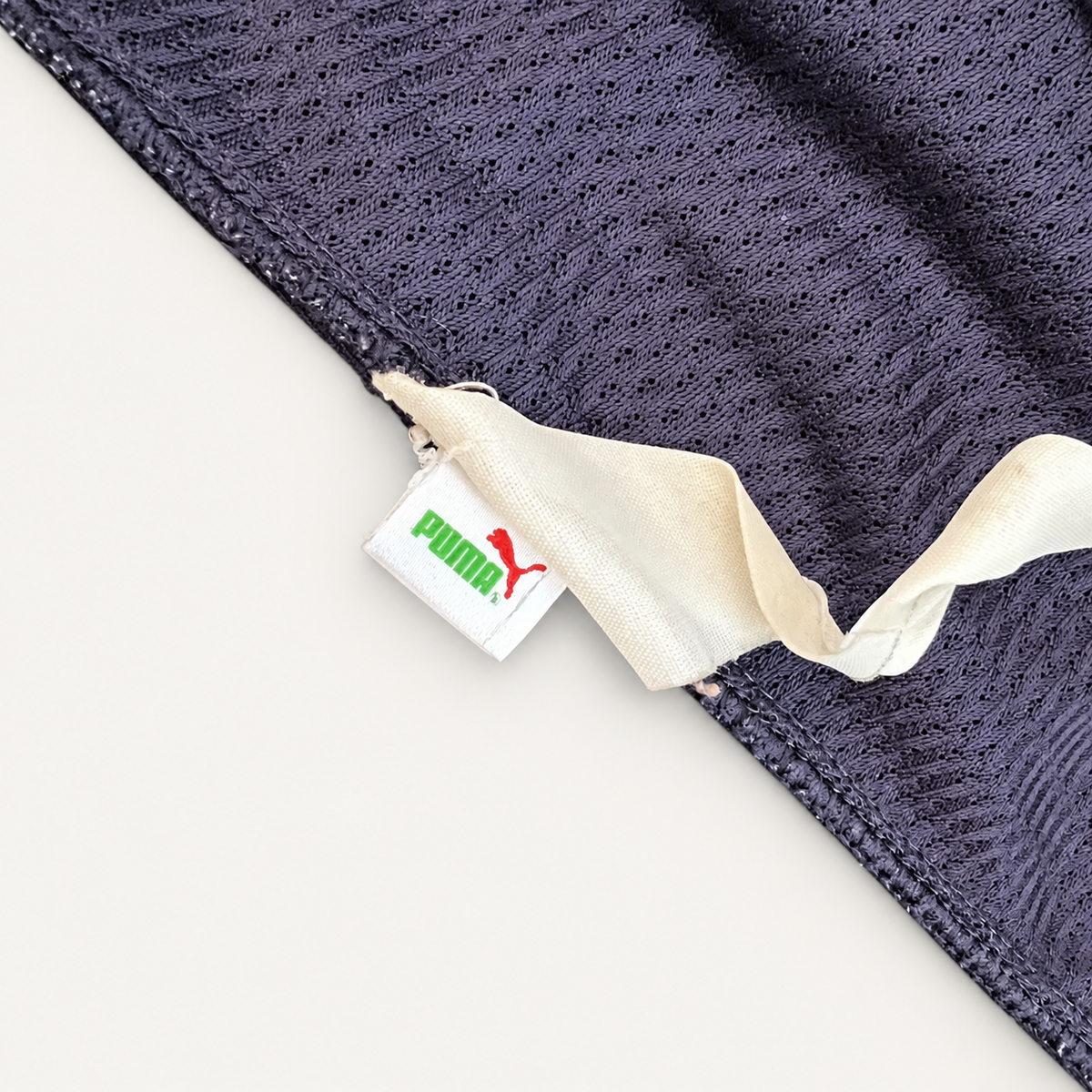 Close-up of a dark navy mesh fabric product with a white fabric tab and a visible Puma tag featuring the green Puma wordmark and red leaping cat logo.
