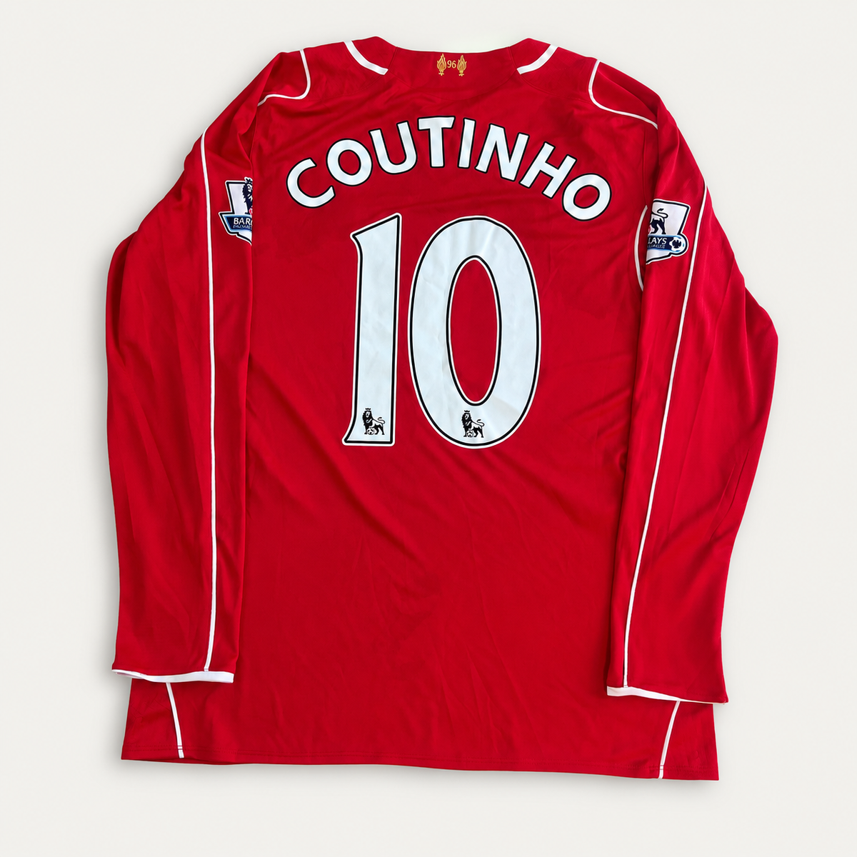 A red long-sleeve soccer jersey laid flat on a light background, showing the back with 'COUTINHO' and the number '10' in white. The jersey has white piping along the shoulders and sleeves, and a small crest near the bottom right hem.