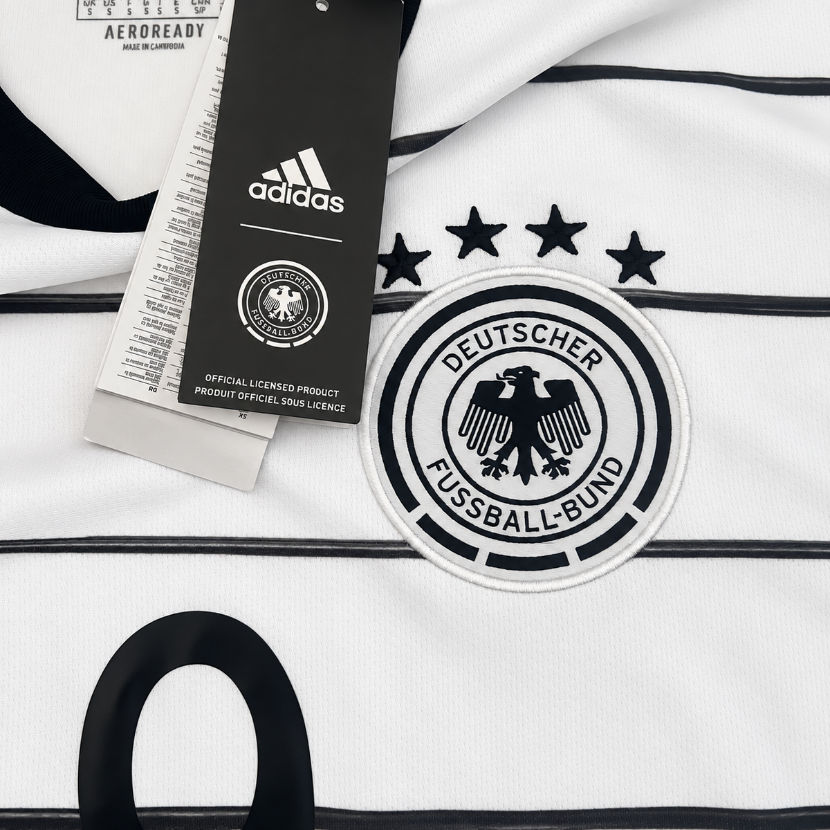 A close-up of a white Adidas Germany soccer jersey with black pinstripes, featuring the circular Deutscher Fußball-Bund crest, three black stars, and a black Adidas hangtag.