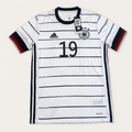 A white Adidas Germany soccer jersey with black vertical stripes, the number 19 on the chest, and black, red, and gold trim on the collar and cuffs, shown flat on a light beige background.